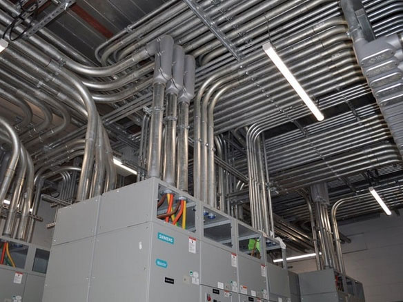 A spacious room filled with numerous electrical wires and pipes running along the walls and ceiling.